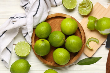 Wall Mural - Plate and cutting board with fresh ripe limes on white wooden background