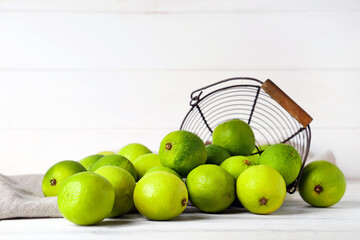 Wall Mural - Basket with fresh ripe limes on white wooden background