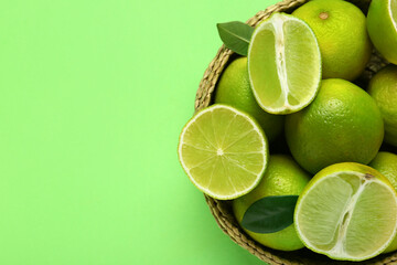 Wall Mural - Wicker basket with fresh ripe limes and leaves on green background