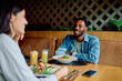 © we.bond.creations - Young multicultural couple laughing over a casual daytime dinner at a modern restaurant, sharing pasta, salad and drinks, relaxed togetherness