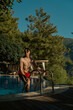 © ALPSARAL - Poolside Relaxation: A fit person climbs out of the clear blue water of a luxurious pool, against a backdrop of natural scenery. capturing moments of relaxation and leisure