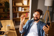 © Stockphotodirectors - A man sits at a wooden desk in a home office, wearing headphones and smiling while holding a smartphone. Sunlight filters through the room, creating a relaxing atmosphere.
