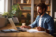 © Stockphotodirectors - A man is engaged in work at a comfortable home office, taking notes on paper while using a laptop, surrounded by plants and organized bookshelves during the afternoon.