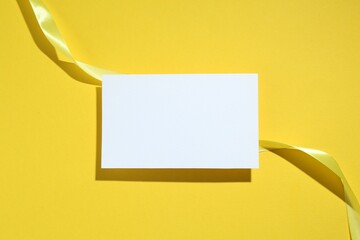 Wall Mural - Beautiful ribbon and blank card on yellow background, flat lay