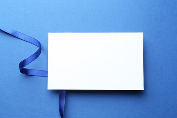 Wall Mural - Beautiful ribbon and blank card on blue background, flat lay