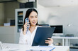 © Nuttapong punna - Asian Business woman Talking on the phone and using a laptop with a smile while sitting at office