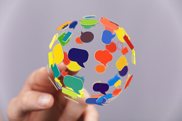 Wall Mural - Hand holding global sphere made of colorful speech bubbles, representing communication, social media, and connection in a modern world.