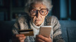 © Techno Stoks - scared elderly woman holding a credit card, using a smartphone to do online shopping on a mobile app