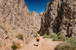 © EdNurg - Female tourist with orange backpack walking on a gravel road in Charyn Canyon, Kazakhstan, on a sunny summer day