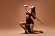 © New Africa - Gymnastics. Woman in sportswear posing on pouf against pale brown background, space for text