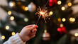 © photo for everything - Child's hand holding a sparkler with a Christmas tree in the background, festive holiday celebration, and a glowing light, fun activity