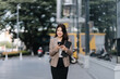 © Kritdanai - City Stroll: A sophisticated young woman strides confidently through a bustling urban landscape.