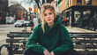 © hdesert - Casual young woman wearing a green hoodie, sitting on a city bench, relaxed urban vibe
