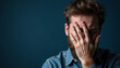 © AlenaSi - Depressed man covering face in despair against dark blue background, symbolizing sorrow. Depressed man feels emotional pain and mental anguish, covering face to express his inner turmoil.