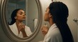 © Mid - Elegant woman with braided hair applies perfume in a warmly lit bathroom. She gazes into a round mirror, holding the bottle gracefully, enhancing her everyday beauty routine in her home.