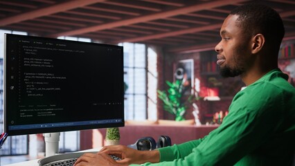 Male programmer types code on computer and running script, programming language. African american IT expert in modern loft fixing errors within the software, implementing new features. Camera A.