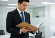 © Arrhman - Asian businessman in suit reading documents in a folder inside an office.