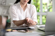 © amenic181 - Young Asian Businesswoman suffering from wrist pain while working on computer, Businesswoman massaging her hand and wrist after long hours in front of a computer, Healthcare office syndrome concept