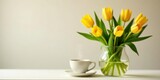 A serene morning scene featuring a cup of steaming beverage and a bouquet of vibrant yellow tulips in a clear glass vase, resting on a pristine white surface against a soft neutral backdrop.