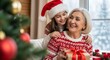 © Ali Raza - Joyful granddaughter wearing a santa hat hugs her smiling grandmother who is holding a christmas gift in front of a decorated tree and window