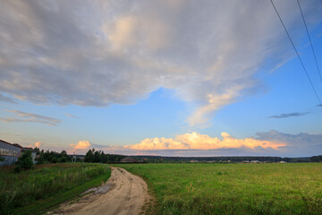 Wall Mural - Road runs through a field with a cloudy sky above