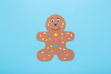 Wall Mural - Brown gingerbread man shape with colorful sprinkles created from multicolor application paper on light blue table background. Pastel color. Making decoration element. Closeup. Top down view.