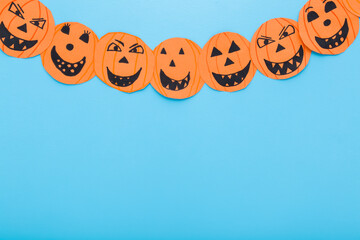 Wall Mural - Orange dark black scary smiling pumpkin faces on light blue table background. Pastel color. Closeup. Creating Halloween decoration. Child handcraft. Empty place for text. Top down view.