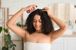 © Pixel-Shot - Beautiful young happy African-American woman applying cosmetic oil on her healthy curly hair in bathroom
