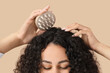 © Pixel-Shot - Beautiful young African-American woman using scalp massager for her healthy curly hair on beige background, closeup