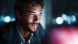 © Bussakon - A young man gazes intently at a glowing computer screen in a dimly lit room with blurred city lights in the background