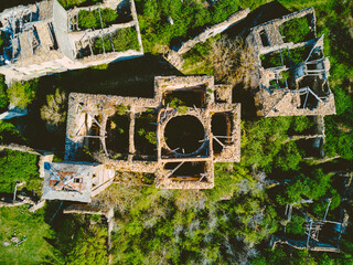Aerial view of the crumbling stone ruins of an old building amidst verdant trees and grass creating a stark contrast between the man-made structure and nature, Mediano, AragÃ³n, Spain.