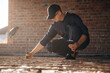 © standret - Sitting and using leveling tool. Builder is working on construction site, unfinished building