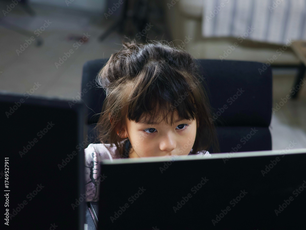 Image of a young girl staring at a computer screen with a serious gaze ...