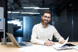 © Tetiana - Portrait of a smiling young man working in the office. Sitting at a desk, working on a laptop and with documents