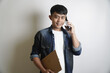 © yashis007 - Young man in casual attire conversing on smartphone while holding file folder