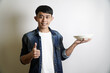 © yashis007 - Smiling young Asian man in a denim jacket holding an empty white plate and giving a thumbs up gesture of approval for good food