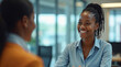 © Maryna - Smiling black woman chats with another person in office setting. Happy, friendly female employee smiles with customer or colleague. Face-to-face communication at work.