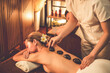 © InfiniteFlow - Hot stone massage at spa salon in luxury resort with warm candle light, blissful woman customer enjoying spa basalt stone massage glide over body with soothing warmth. Quiescent