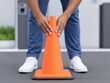© alsu0112 - Individual placing an orange traffic cone on a gray surface, demonstrating safety measures in urban environments, emphasizing traffic management and public safety awareness