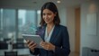 © mian - Businesswoman in a suit holding a tablet with a holographic display in a modern office space