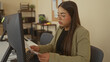 © Krakenimages.com - Woman reading documents in modern office setting, wearing glasses, concentrating at a desk with computer monitor and organized shelves in background.