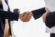 © David - Two business people professionals shaking hands in office setting, sealing a deal with laptop and financial graphs visible. Business handshake over laptop and reports