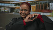 © Krakenimages.com - African american woman in black robe and red blouse smiles and forms heart with hands on street in daylight; love.