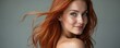 © Oleksandr - Woman with vibrant red wavy hair turns her head to smile. Her natural beauty is evident in this studio portrait, exuding confidence and allure. The wind gently blows strands of her luxurious hair.
