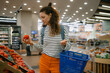 © wifesun - Woman choosing fresh tomatoes from the produce section in a grocery store, shopping for healthy food and picking organic vegetables to prepare nutritious meals