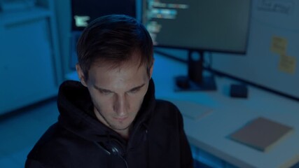 Professional male programmer working night shift in IT room, coding and testing software on multiple monitors, analyzing project data and debugging code, showcasing innovation and technology.