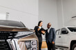 © wedmoments.stock - A male auto consultant and a female customer discuss a car's specifications in a well-lit showroom, demonstrating a high level of customer service and professionalism.