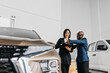 © wedmoments.stock - An African American man and a dealer discuss car features in a modern showroom, focusing on customer service and automotive design.