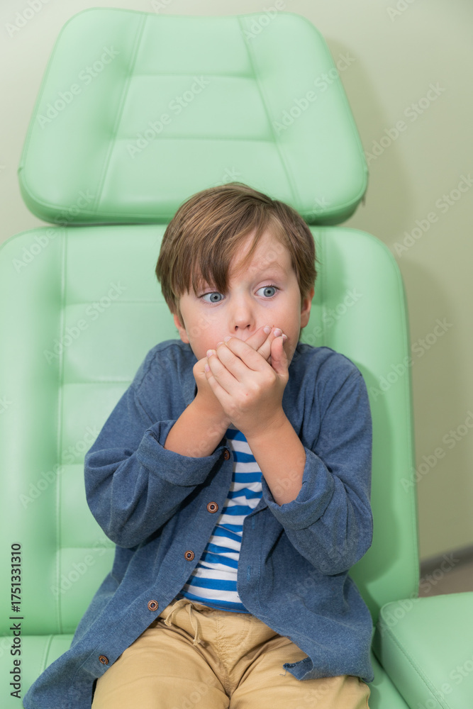 The boy in the doctor's chair is afraid to show his mouth, throat