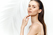 © VICHIZH - Elegant young woman with natural beauty, showcasing smooth skin and a serene expression, against a soft white background with delicate palm leaves.
